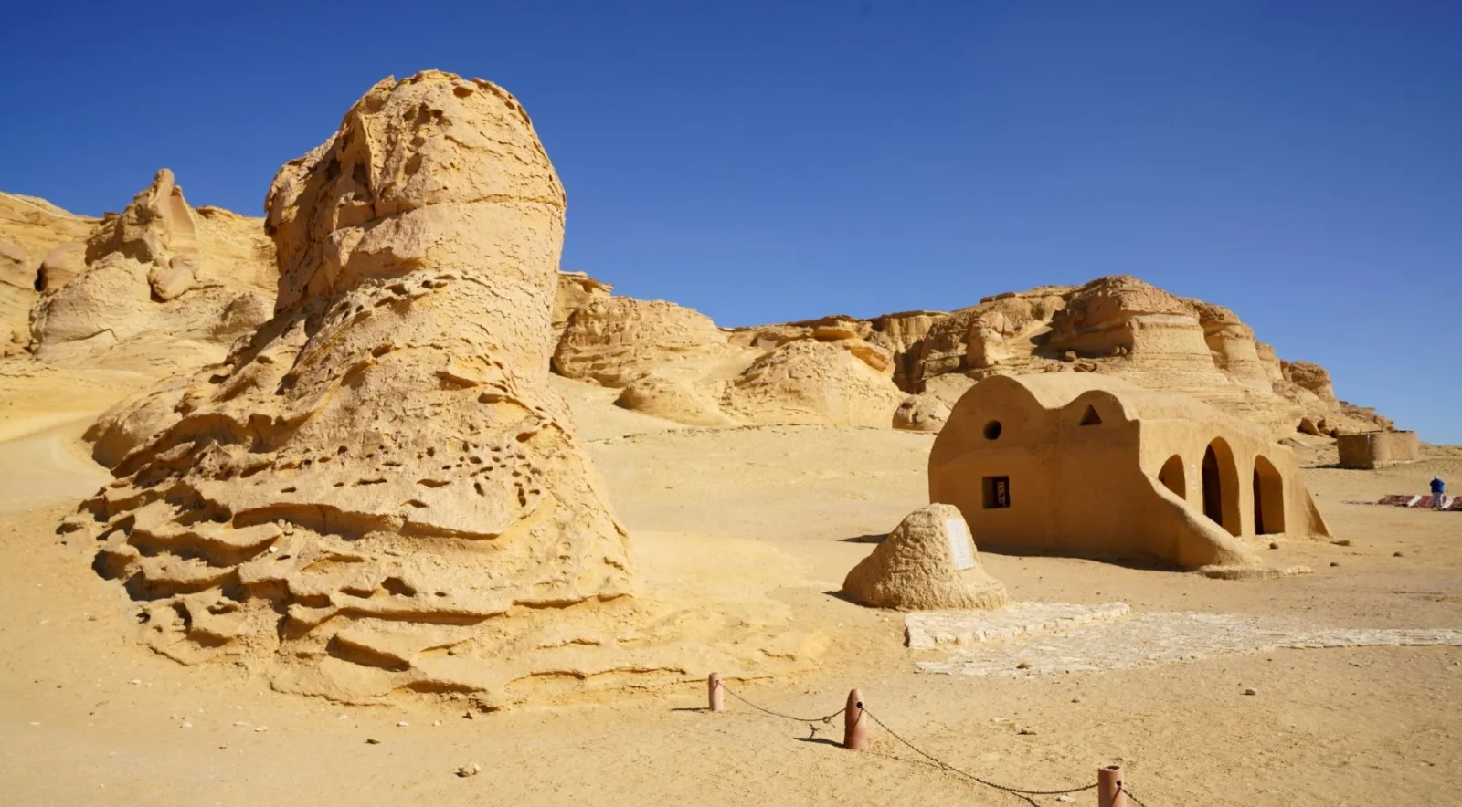 Wind-carved sandstone outcrop beside a domed mud-brick shelter in the southern Tunisian desert