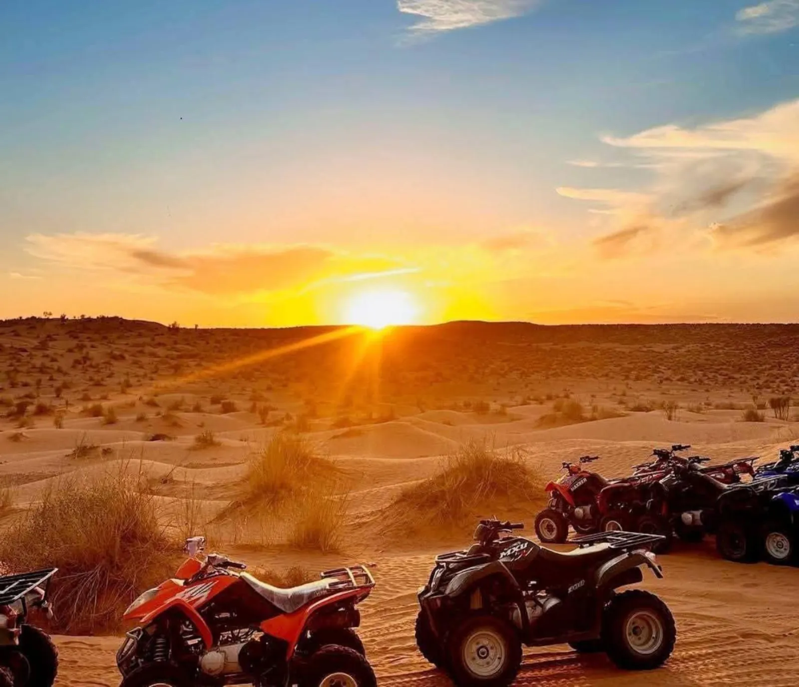 Quad bikes lined up on the sand as the sun drops behind the dunes