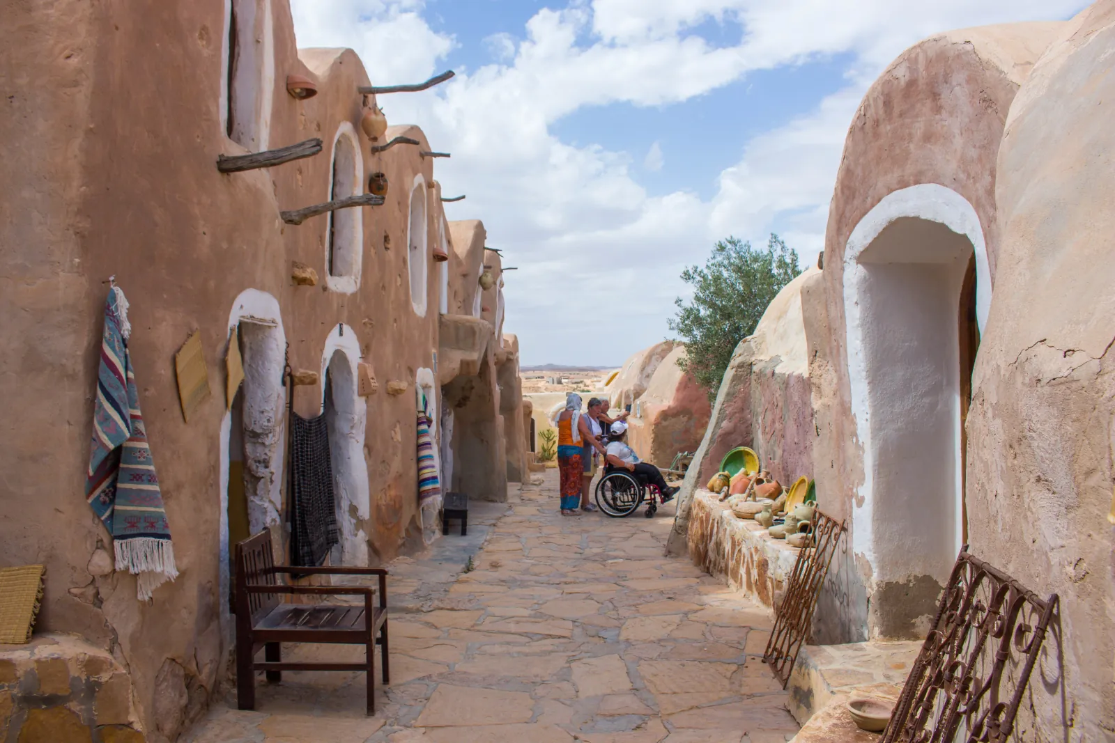 Visitors walking the Ksar Hadada lane past pottery and woven rugs hung on the walls