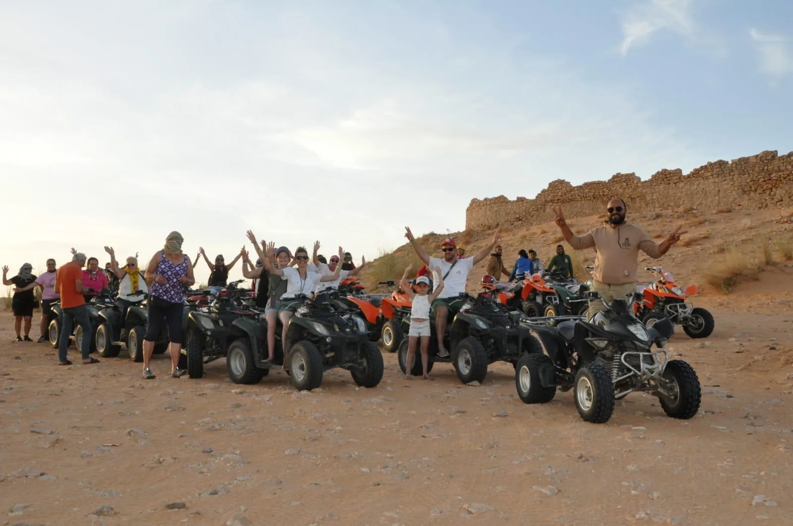 A tour group posing with their quad bikes below the stone wall of a desert ksar