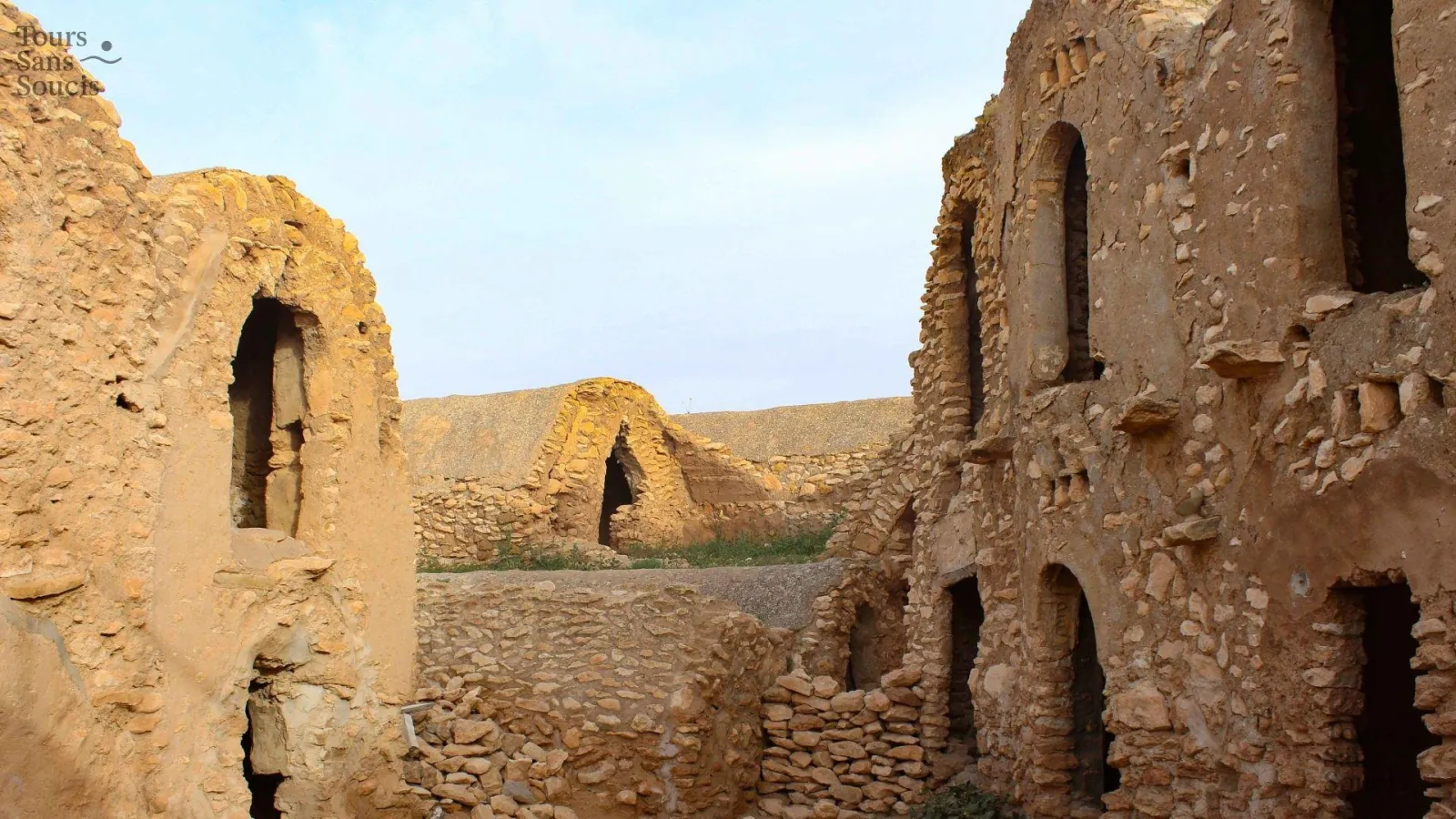 The open courtyard of a ruined ksar, tiers of vaulted granary cells on both sides