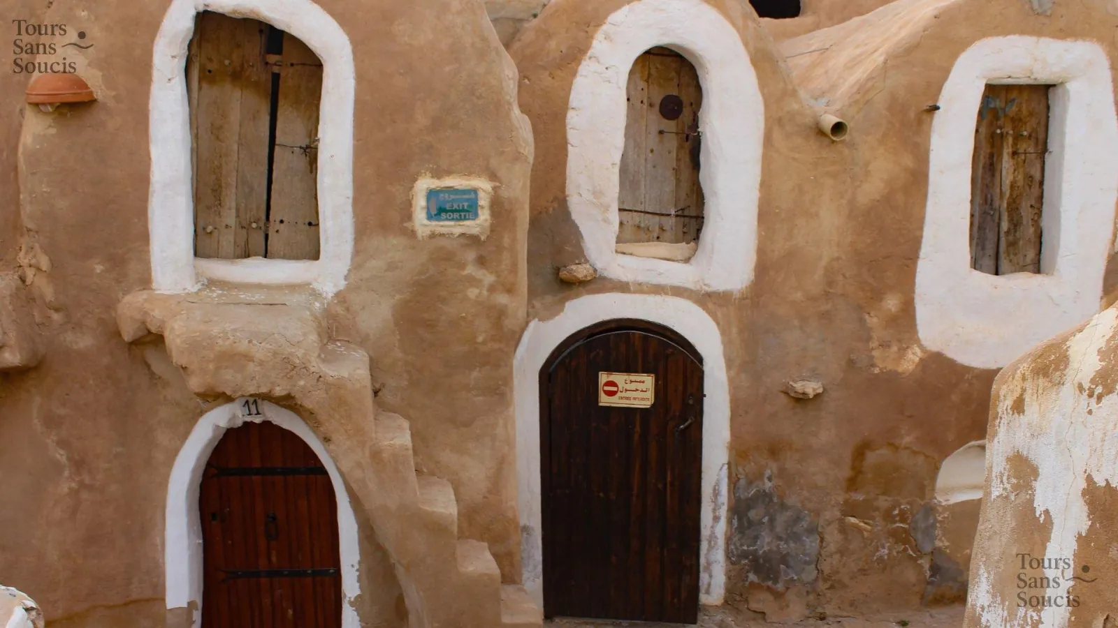 Ksar doors and shuttered openings with a bilingual exit sign on the wall