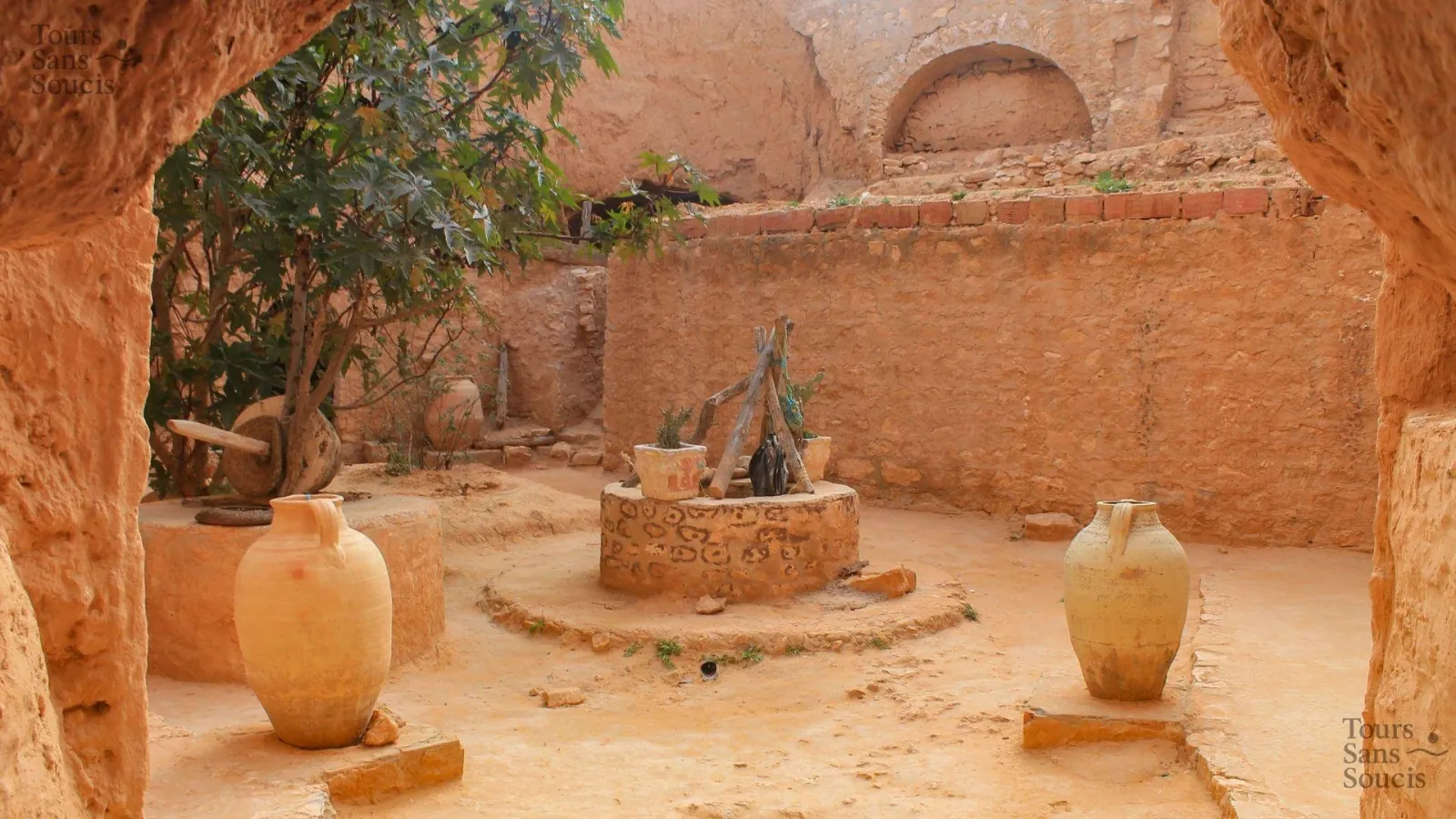 A troglodyte courtyard with its well, olive-press wheel and two tall storage jars