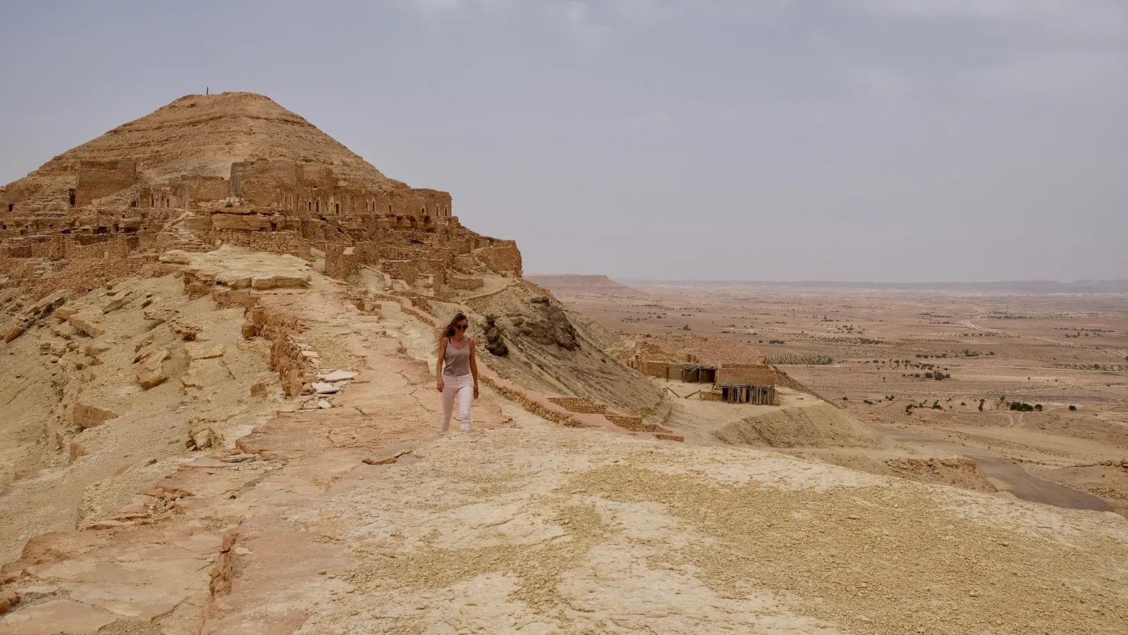 Walking the stone ridge path at Chenini with the desert plain stretching away below